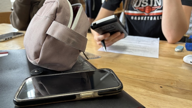 Un élève assis à un bureau avec une calculatrice dans les mains et un téléphone sur son bureau.