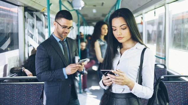 Deux personnes consultent leur téléphone intelligent dans le transport en commun. 