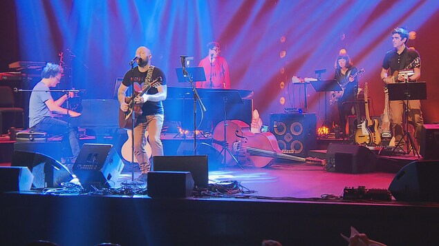 Marco Caliari chante sur scène, entouré de musiciens.