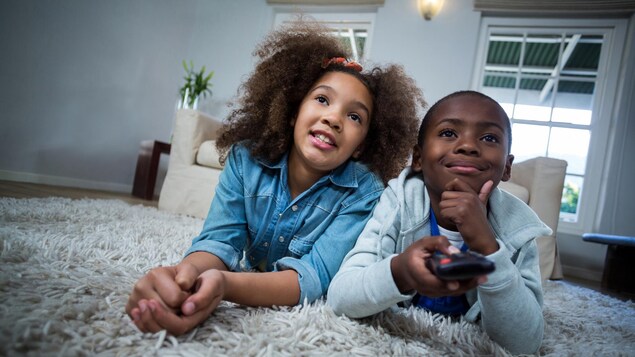 Deux jeunes étendus sur le ventre sur un tapis dans un salon, l'un d'entre eux tient une télécommande.
