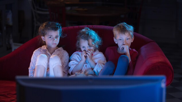 Trois enfants sur un canapé chez eux, regardent un film