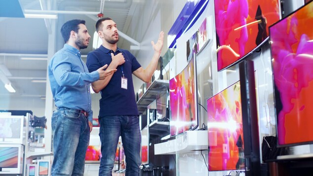 Un vendeur présente des télévisions à un client dans un magasin de produits électroniques.