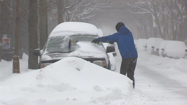 Un homme déneige sa voiture à Montréal.