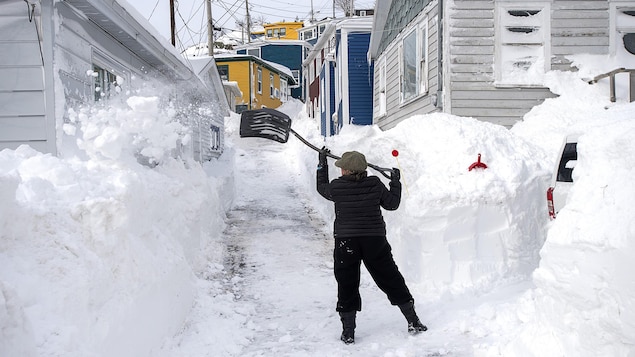 Une femme tente d'enlever la neige de son entrée de maison.