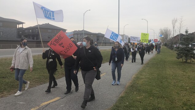 Les infirmières marchent sur la piste cyclable à proximité de l'hôpital, pancartes et drapeaux en mains.