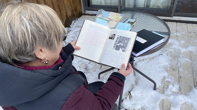 Une femme de dos montrant l'intérieur d'un cahier où se trouve un texte écrit à la main.