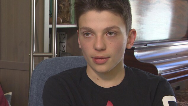 Un adolescent, cheveux foncés et t-shirt noir, assis dans une chaise.