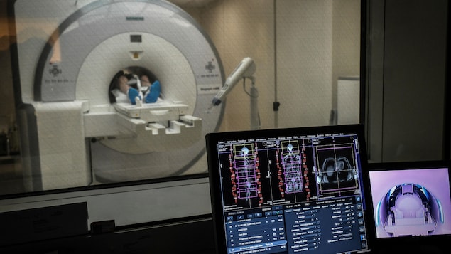 Un patient entre dans un appareil PET Scan alors qu'à l'avant-plan, les premières images de la radiographie apparaissent sur l'écran d'un ordinateur.