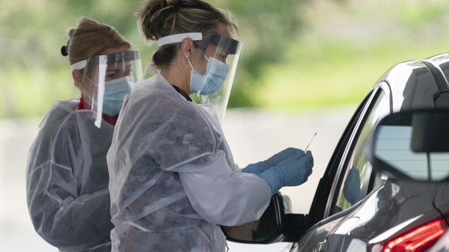 Deux infirmières masquées et gantées s'entretiennent avec un automobiliste.