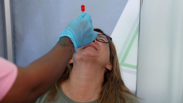 Una mujer con la cabeza inclinada hacia atrás hace una mueca de incomodidad mientras se le toma una muestra de la fosa nasal.
