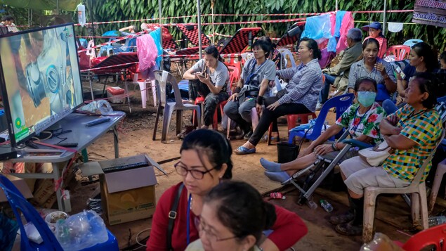 Des gens sont assis sur des chaises de plastique devant une télé dans un camp de fortune. Des gens sont assis sur des chaises de plastique devant une télé dans un camp de fortune.