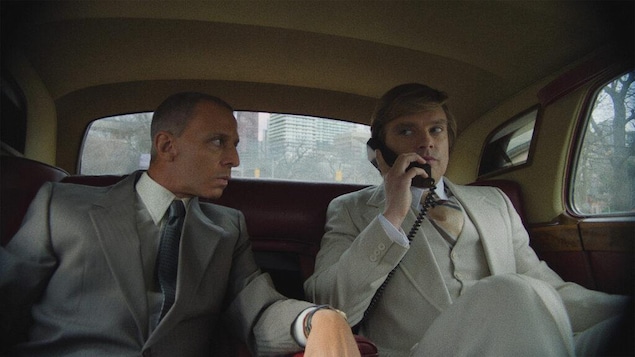 Deux hommes à l'arrière d'une voiture, l'un étant au téléphone. 