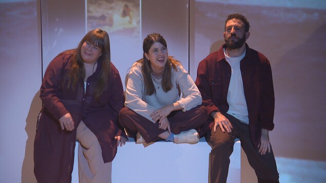 Deux comédiennes et un comédien sourient sur scène. 