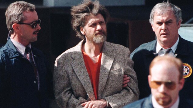 Theodore Kaczynski menotté et entouré de policiers.