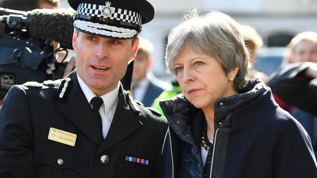 À gauche, un policier britannique vêtu d'une casquette, et à droite, Theresa May. À gauche, un policier britannique vêtu d'une casquette, et à droite, Theresa May.