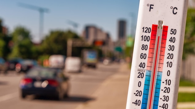 Un thermomètre devant des véhicules qui circulent pendant une canicule à Montréal.