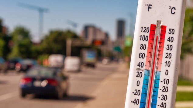 Un thermomètre devant des voitures et de la circulation pendant une canicule à Montréal.