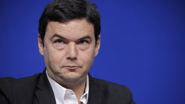 Thomas Piketty l'air sérieux sur fond bleu. 