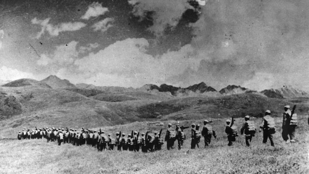 Une photographie d'archive en noir et blanc représentant des troupes chinoises marchant vers la frontière du Tibet dans un paysage montagneux.