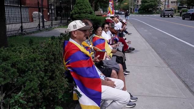 Des personnes drapées dans des drapeaux du Tibet sont assis dans la rue.