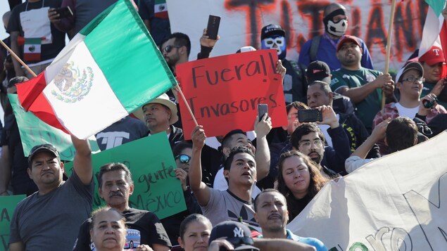 Des gens en groupe brandissent des drapeaux mexicains et des affiches anti-migrants. Des gens en groupe brandissent des drapeaux mexicains et des affiches anti-migrants.