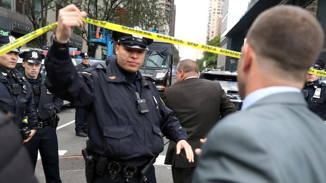 Un policier soulève un ruban de sécurité pour laisser passer une personne.