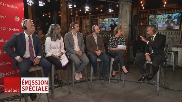Cinq candidats et un animateur assis sur des tabourets dans un bar.