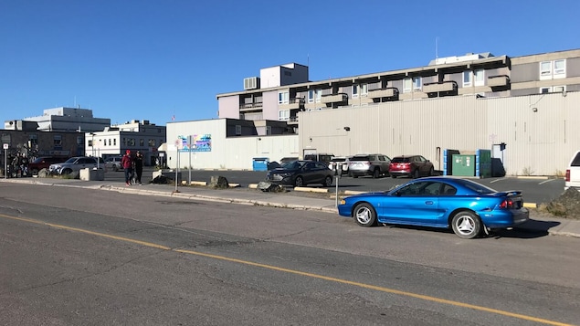 Édifice et rue au centre-ville de Yellowknife, avec voiture stationnée le long d'un terrain vacant.