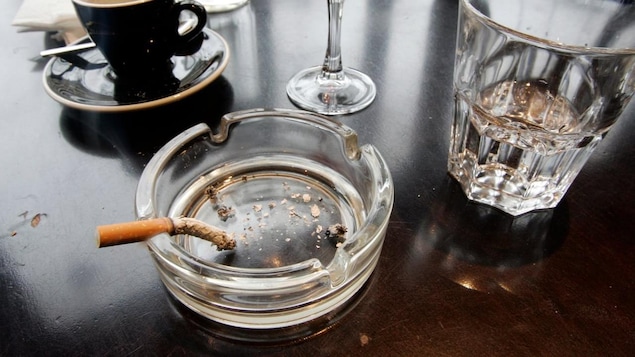 A burnt cigarette in an ashtray next to various glassware and espresson cups.