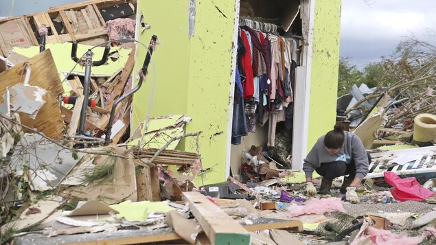 Une femme portant des gants cherche dans les restes d'une maison dévastée par une tornade.