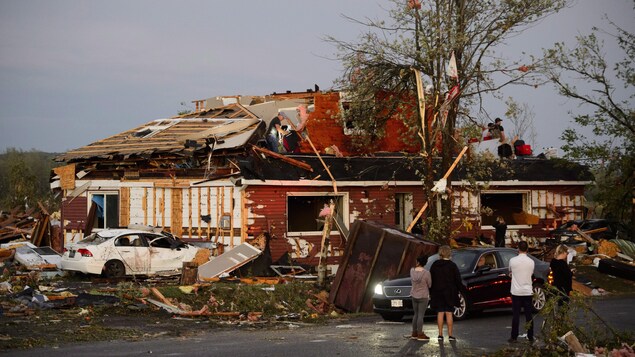Plusieurs personnes sont debout dans la rue ou sur le toit d'une maison en ruines.