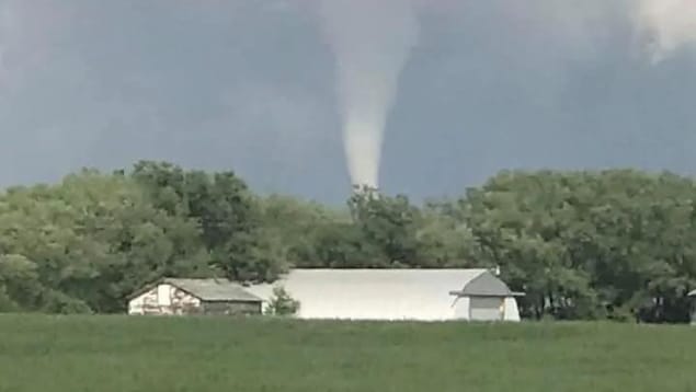 Paysage de campagne au-dessus duquel s'élève un cône de tornade