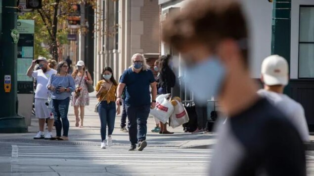 Des gens marchent dans la rue avec un masque.