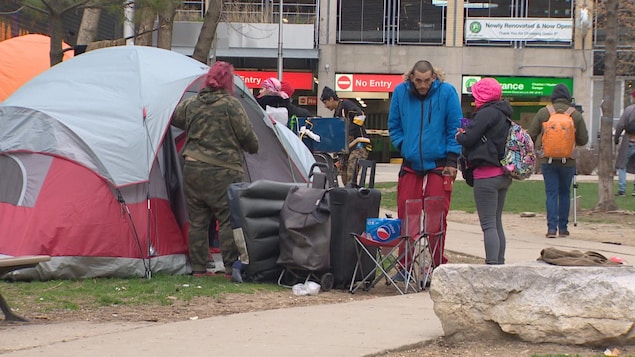 Des sans-abri près d'une tente érigée dans un parc.