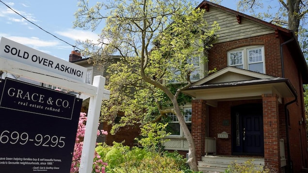 A sold-over-asking sign in front of a brick house.