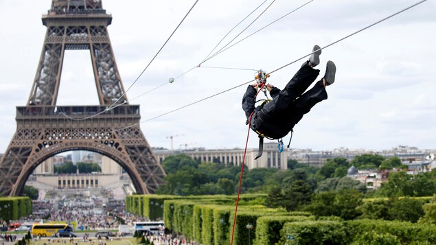 Un homme est suspendu au câble de la tyrolienne de la tour Eiffel. Le câble de la tyrolienne part du deuxième palier de la tour. Le parcours est de 800 mètres et s'arrête près du Mur de la Paix?