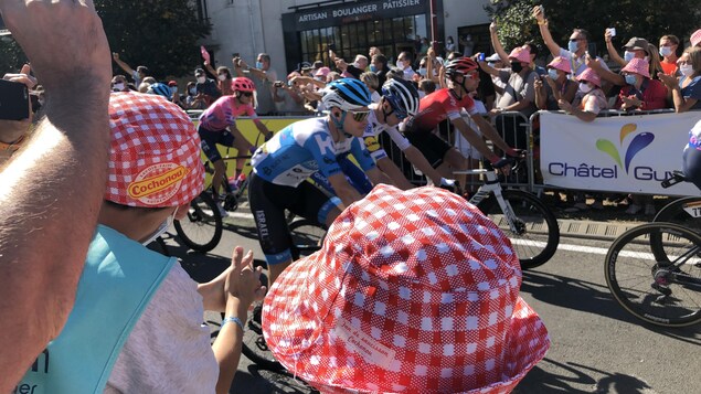 Les gens sont massés près de la route et regardent les cyclistes passer.