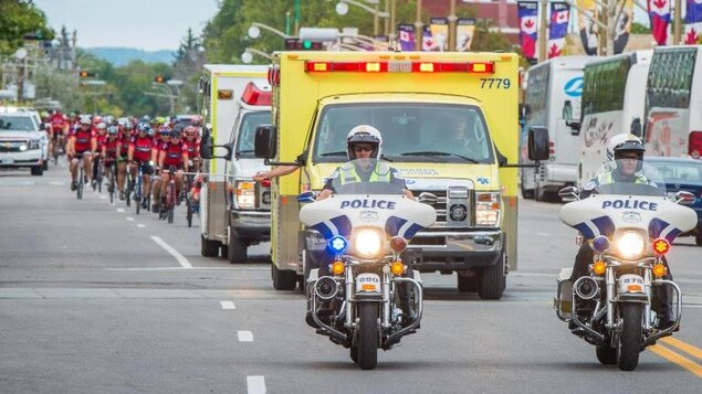 Deux motos de police suivies de deux ambulances et d'un peloton de cyclistes.
