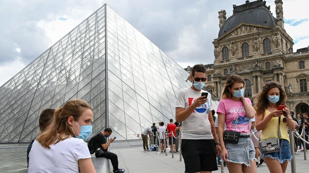 Devant la Pyramide du Louvre, des personnes portent des masques.