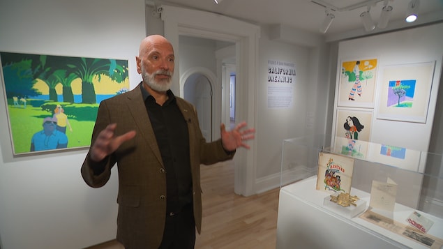 Un homme gesticule dans un musée entouré de peintures colorées. 