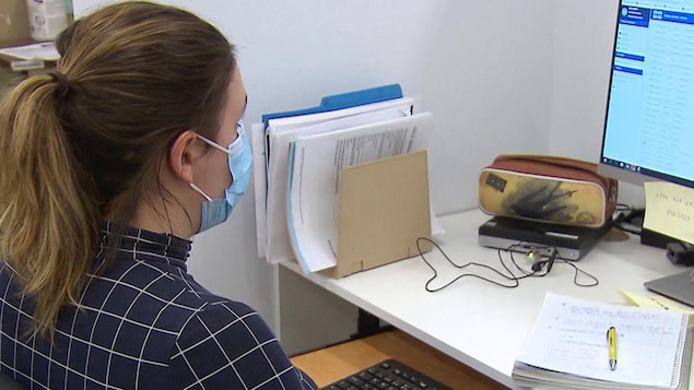 Une femme portant un masque est assise devant son poste d'ordinateur.