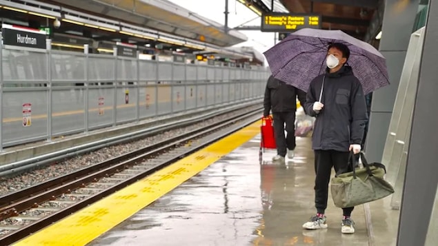 Un usager tenant un parapluie et portant un masque attend le train.