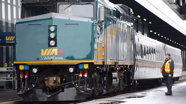 Un employé regarde passer un train de VIA Rail.