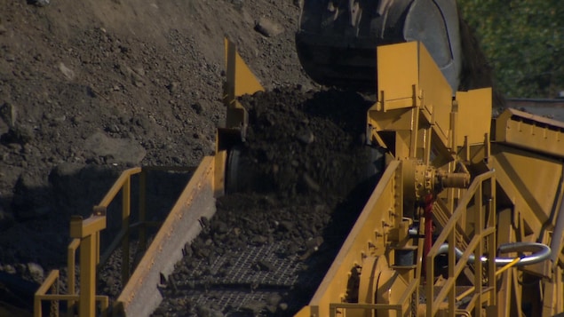 Un convoyeur reçoit des sols contaminés déposés par une grue.