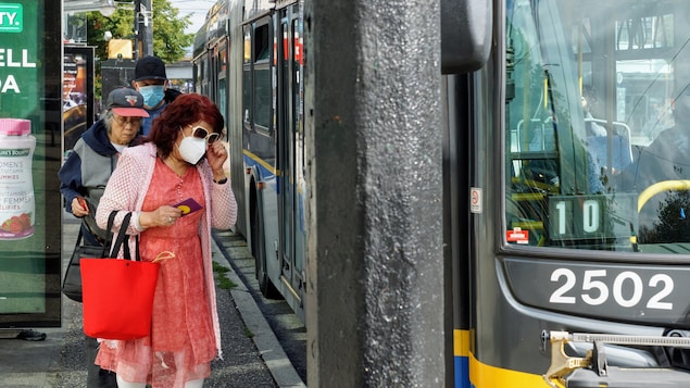 Des usagers munis d'un masque s'apprêtent à prendre un bus Translink.