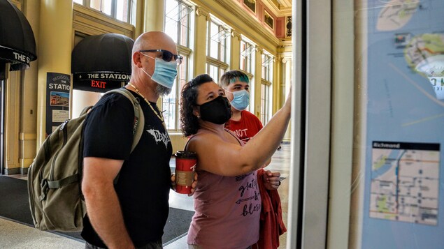 Trois personnes masquées achètent des billets de transport à un distributeur.