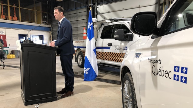 François Bonnardel parle à un lutrin devant deux camionnettes du ministère des Transports.