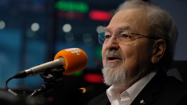 Un homme avec une barbe et des cheveux blancs dans un studio de radio.