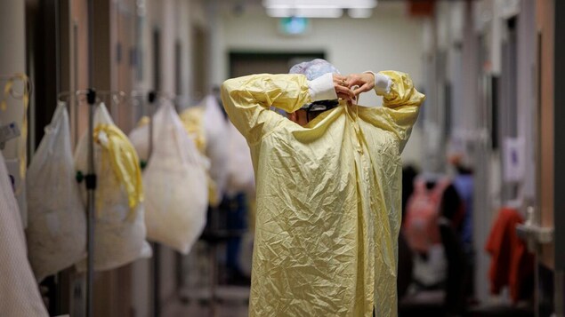 Un travailleur de la santé dans un corridor d'hôpital en train d'ajuster son vêtement protecteur. 