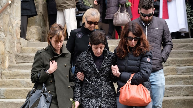 Cinq personnes en deuil descendent les marches de l'église en se tenant par la main.